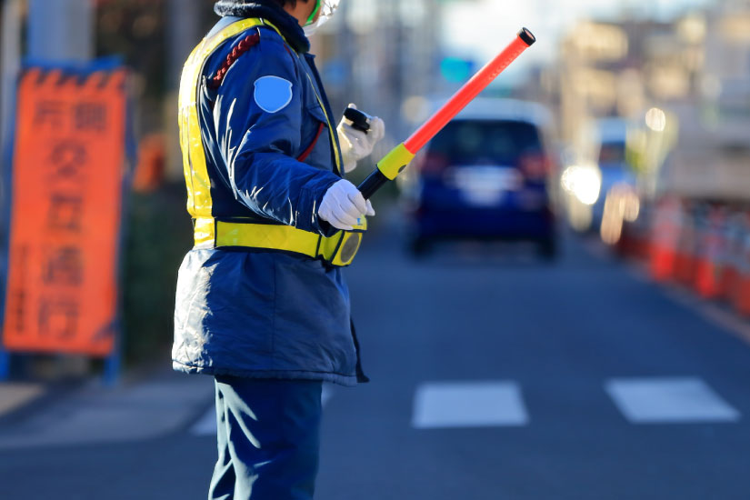 道路工事現場で交通誘導を行う警備員の写真。警備員配置基準の具体例を示すイメージ