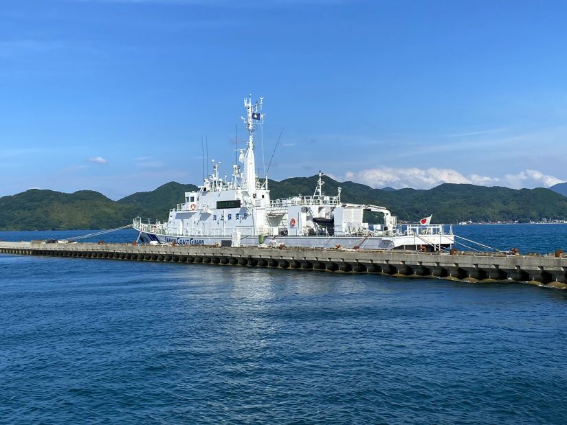 埠頭に停泊している海上保安庁の巡視船「えちぜん」（PM25）が、青い空と緑の山々を背景に写っている。