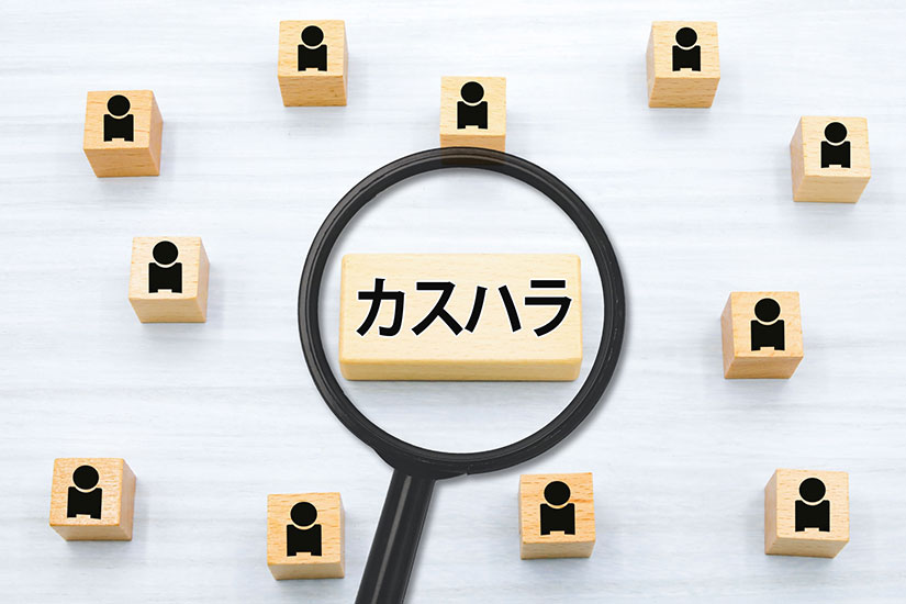カスハラと書かれた木のブロックを虫眼鏡でのぞいている様子